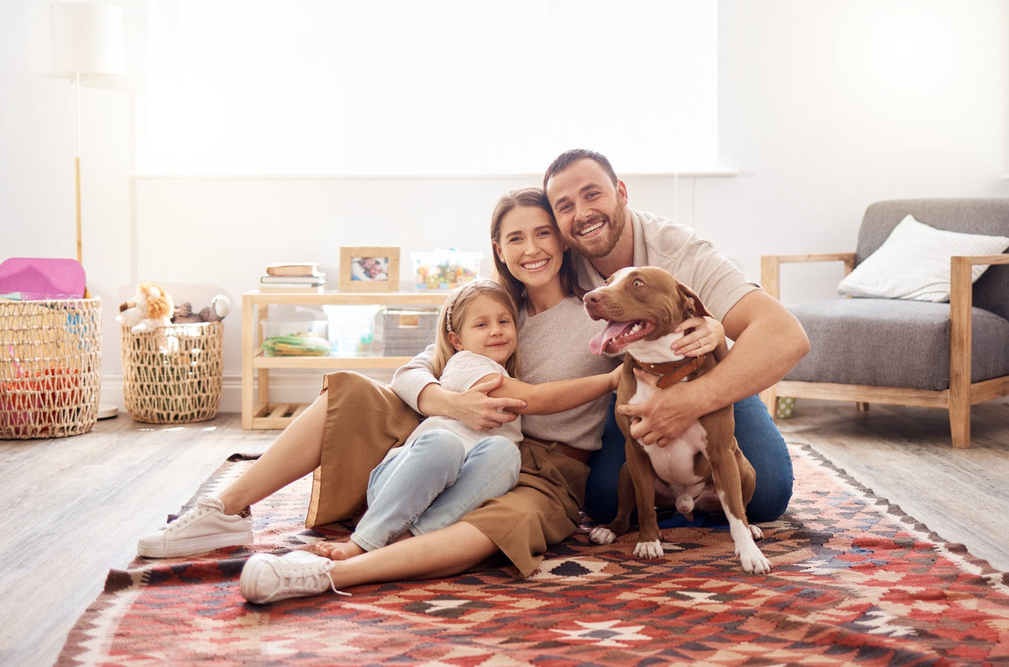 Family of three with a dog sitting on a rug in a living room.